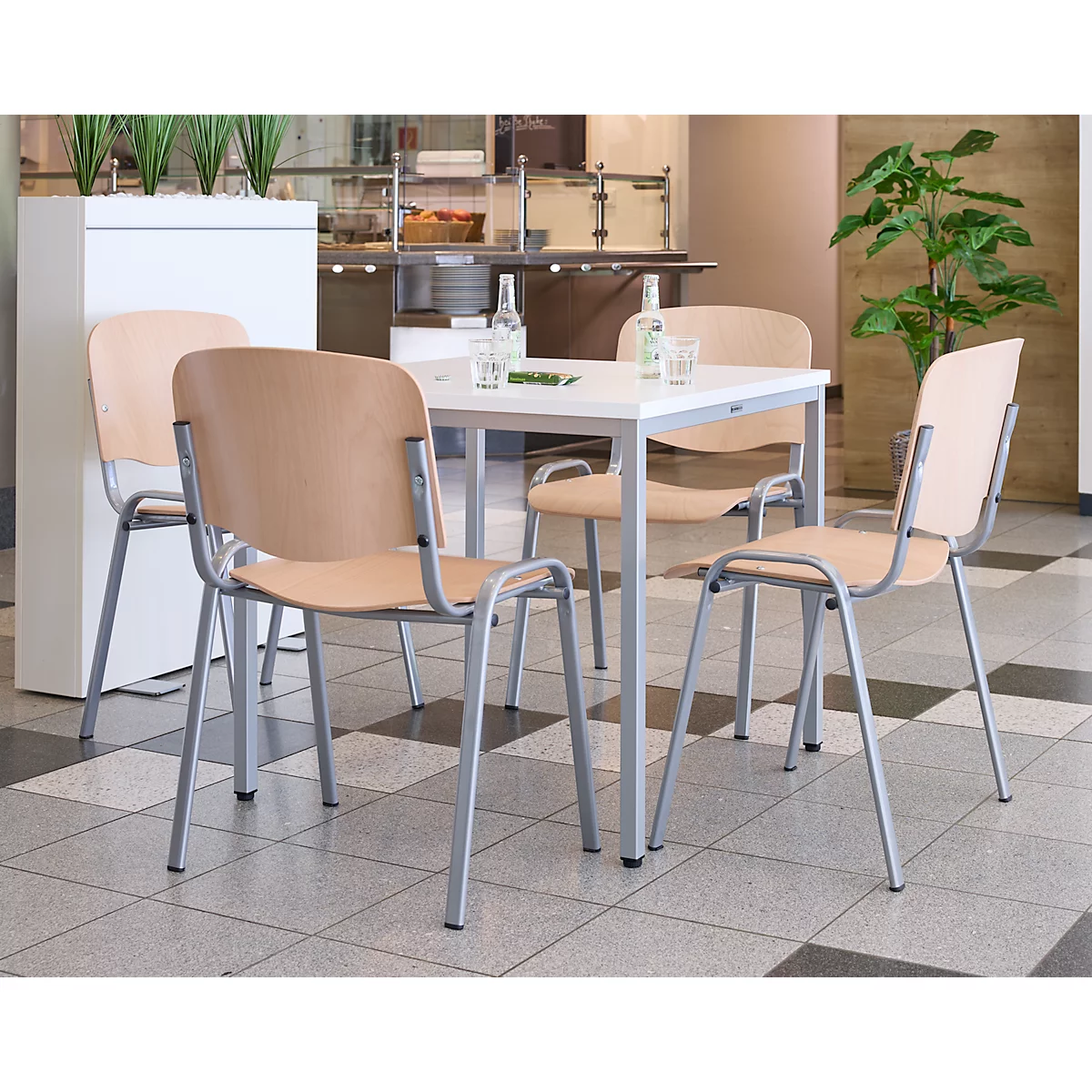 Een tafel met vier stoelen in een eethoek. Licht houten zittingen, zilveren frames. Tegelvloer.