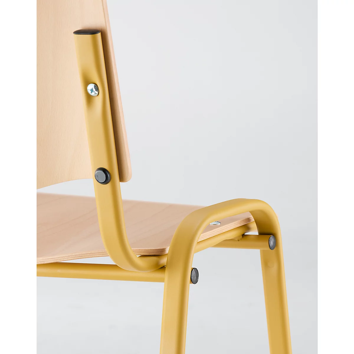 Detailopname van een gele stoel met een houten rugleuning en zitting. Zwarte schroeven verbinden de onderdelen.