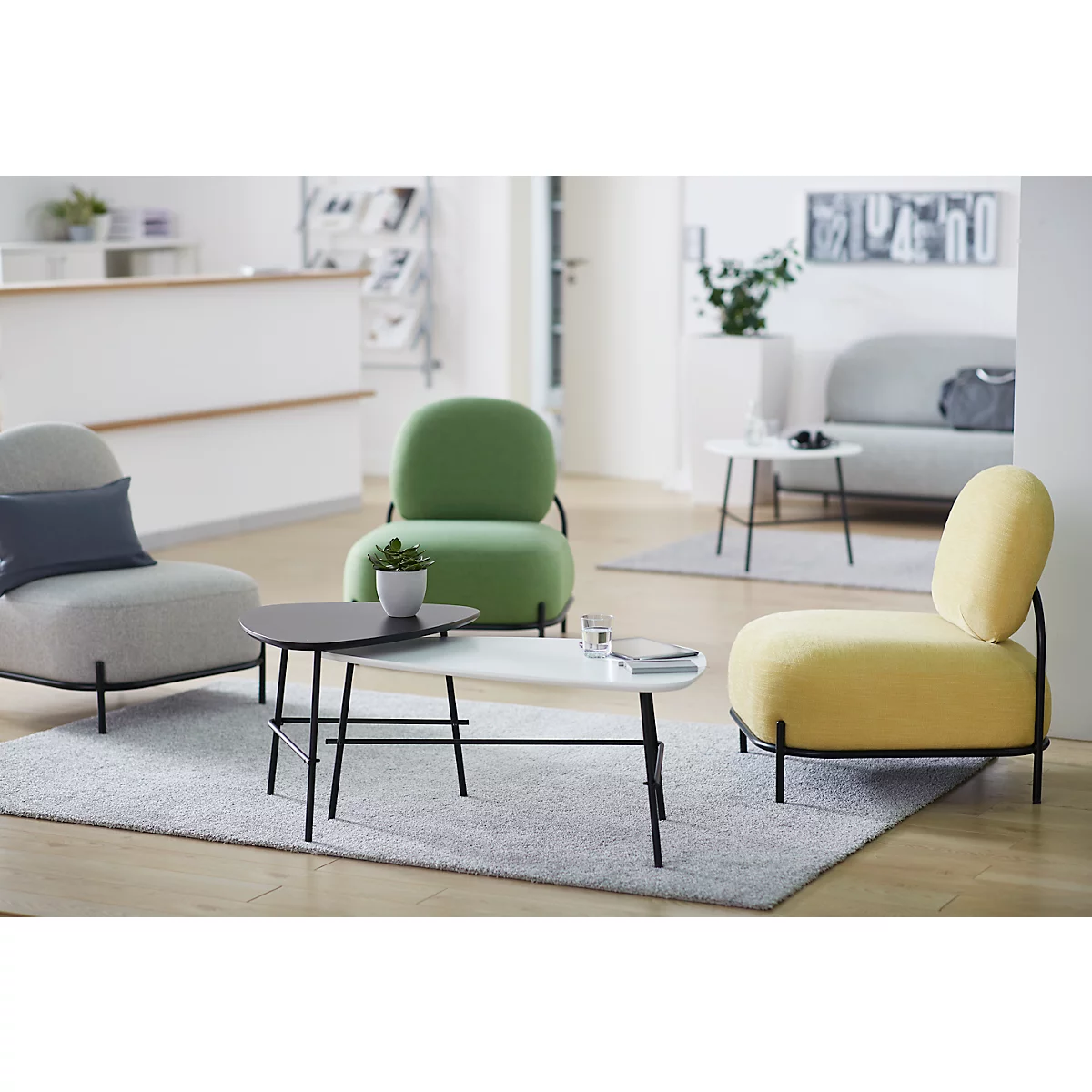 Een gezellige woonkamer met groene, grijze en gele fauteuils, bijzettafels en een licht tapijt.