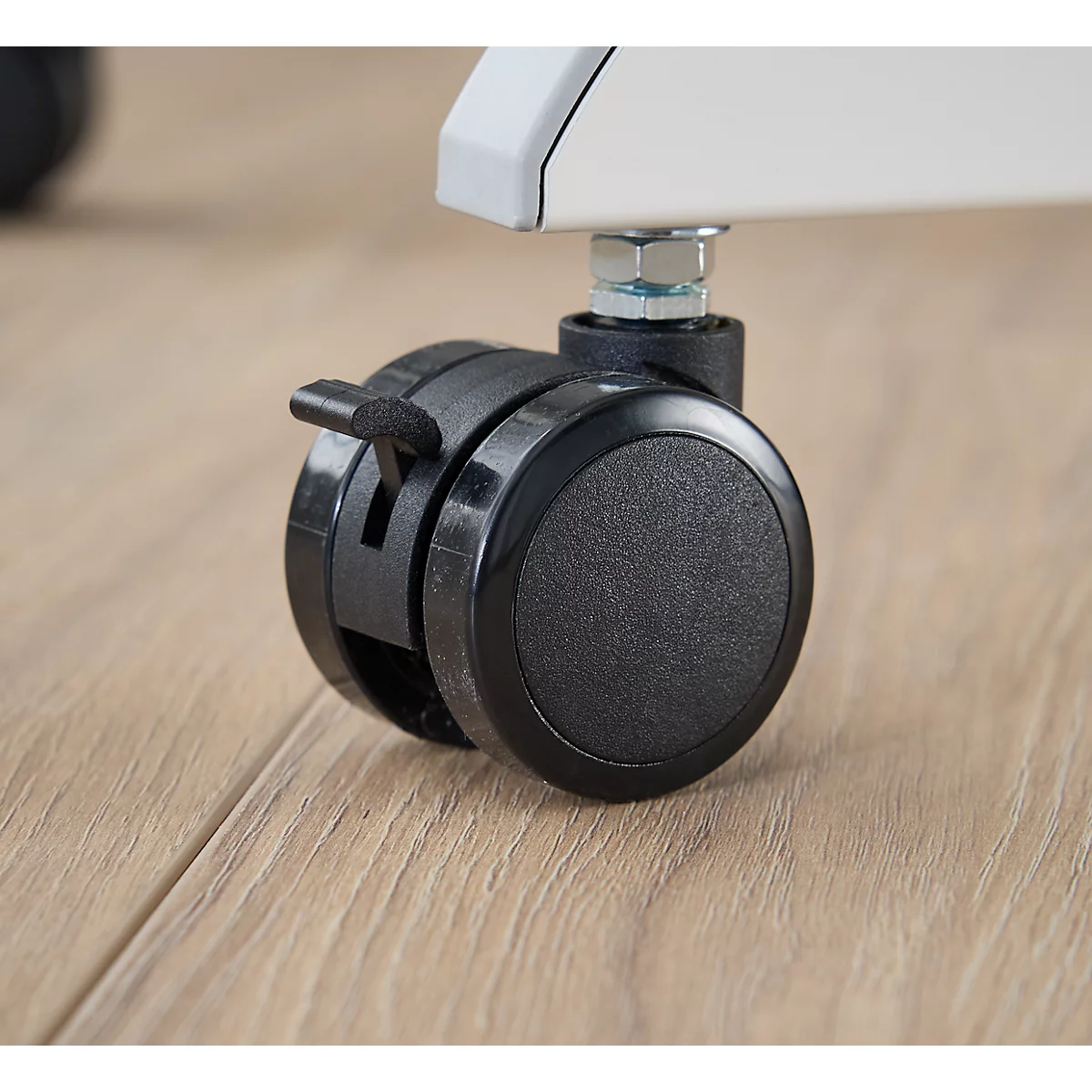 Close-up van een zwart meubelwiel met een vergrendelingshendel. De achtergrond is een houten vloer.