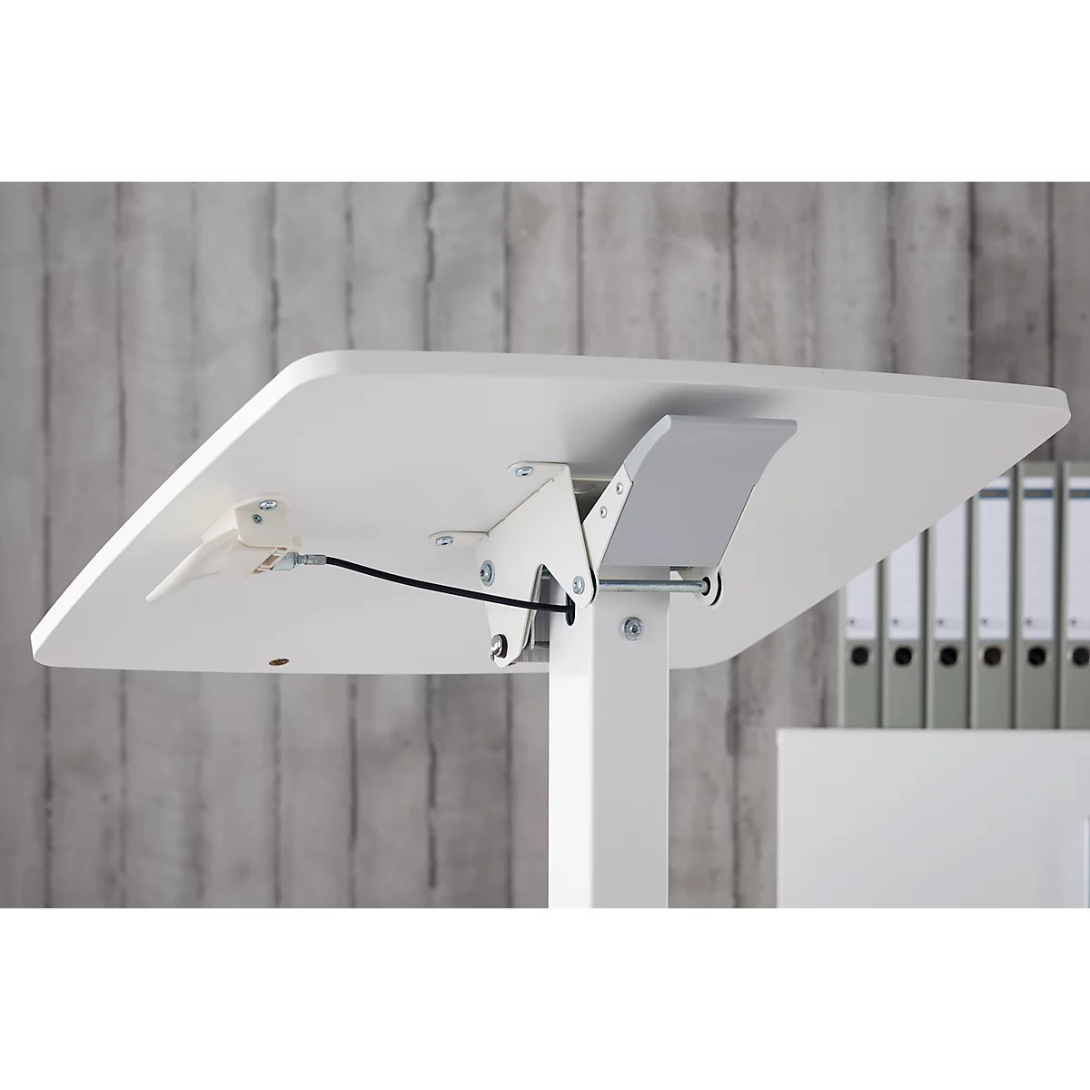 Close-up van de onderkant van de tafel met een wit tafelblad en metalen fittingen. Zwarte kabel zichtbaar.