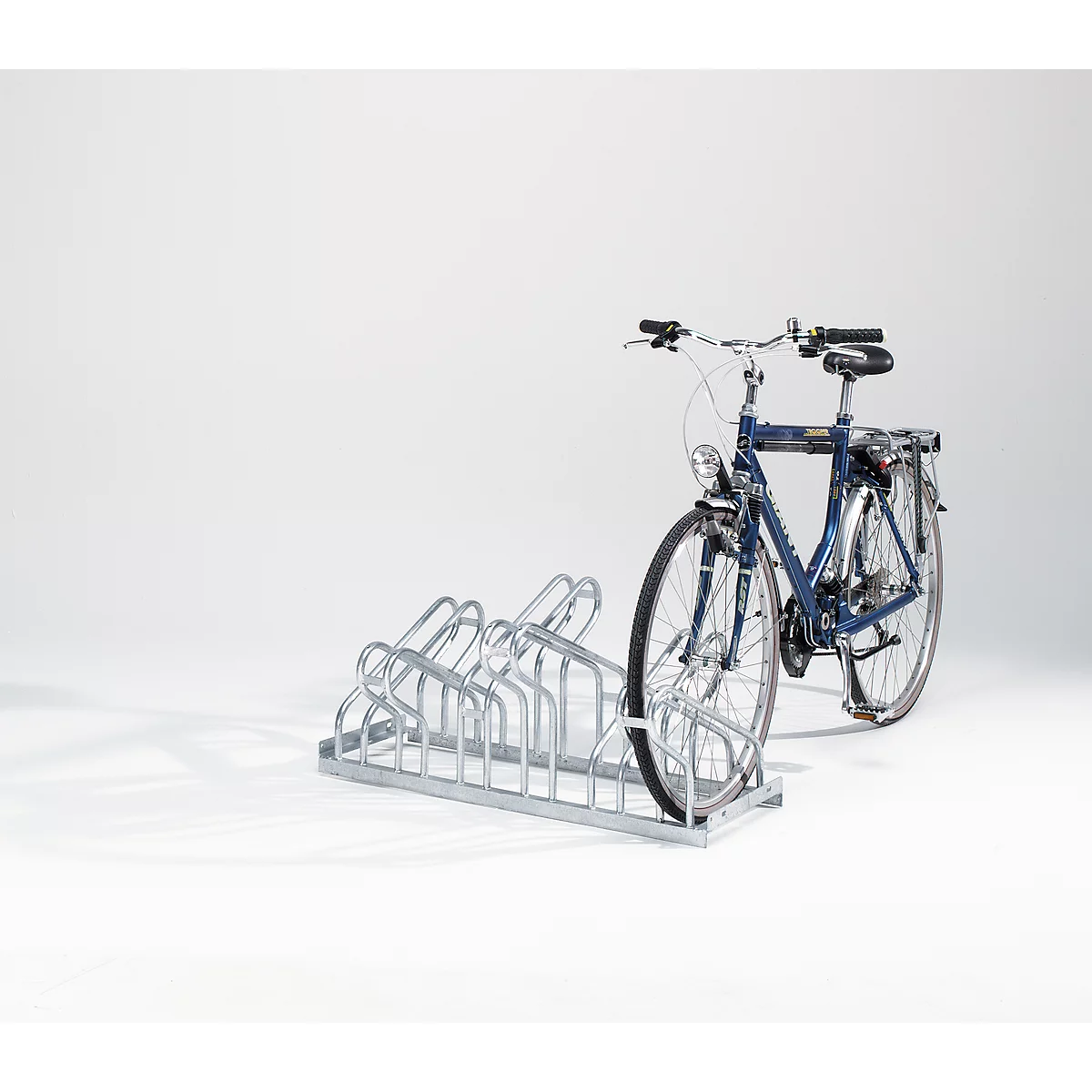 A blue bicycle stands in a metal bicycle rack against a white background.