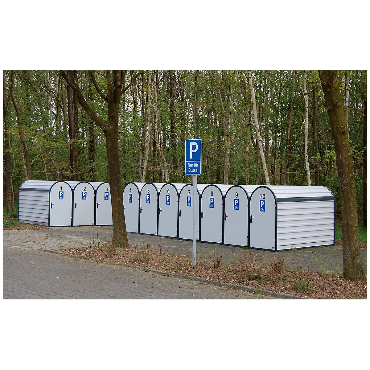 A row of white bicycle garages with blue signs. A parking sign stands in front of a forest background.