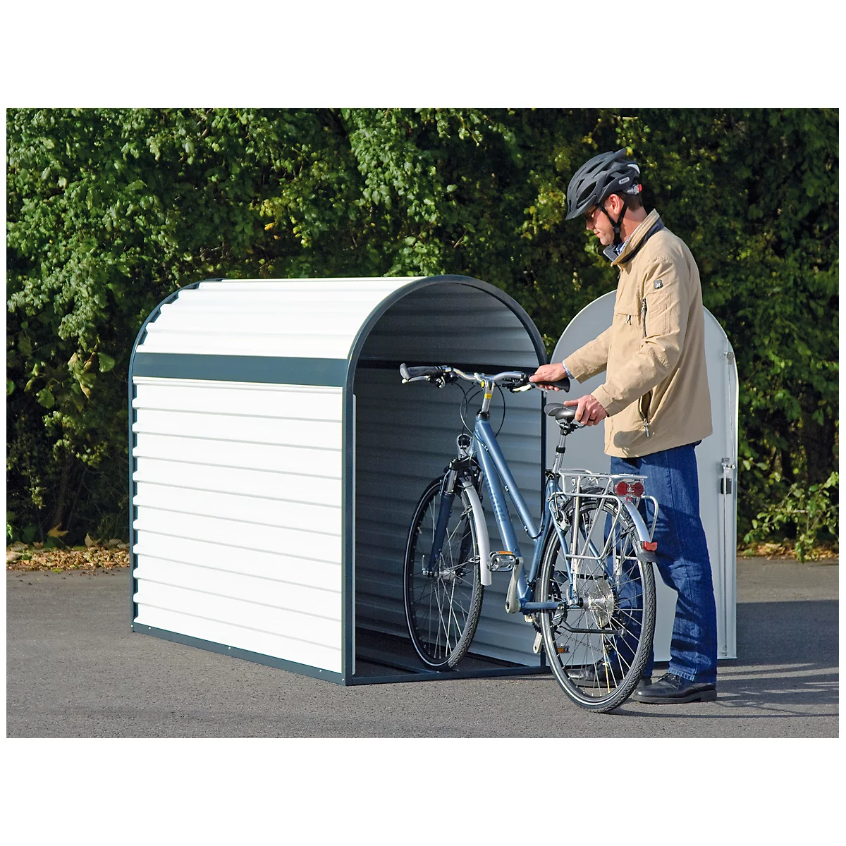 Man putting a bicycle into a white bicycle garage. He wears a helmet and a jacket.