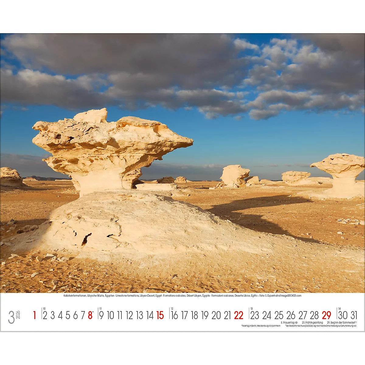 Wüstenlandschaft mit skulpturartigen Felsformationen unter blauem Himmel mit Wolken. Kalender mit März-Datum am unteren Rand.