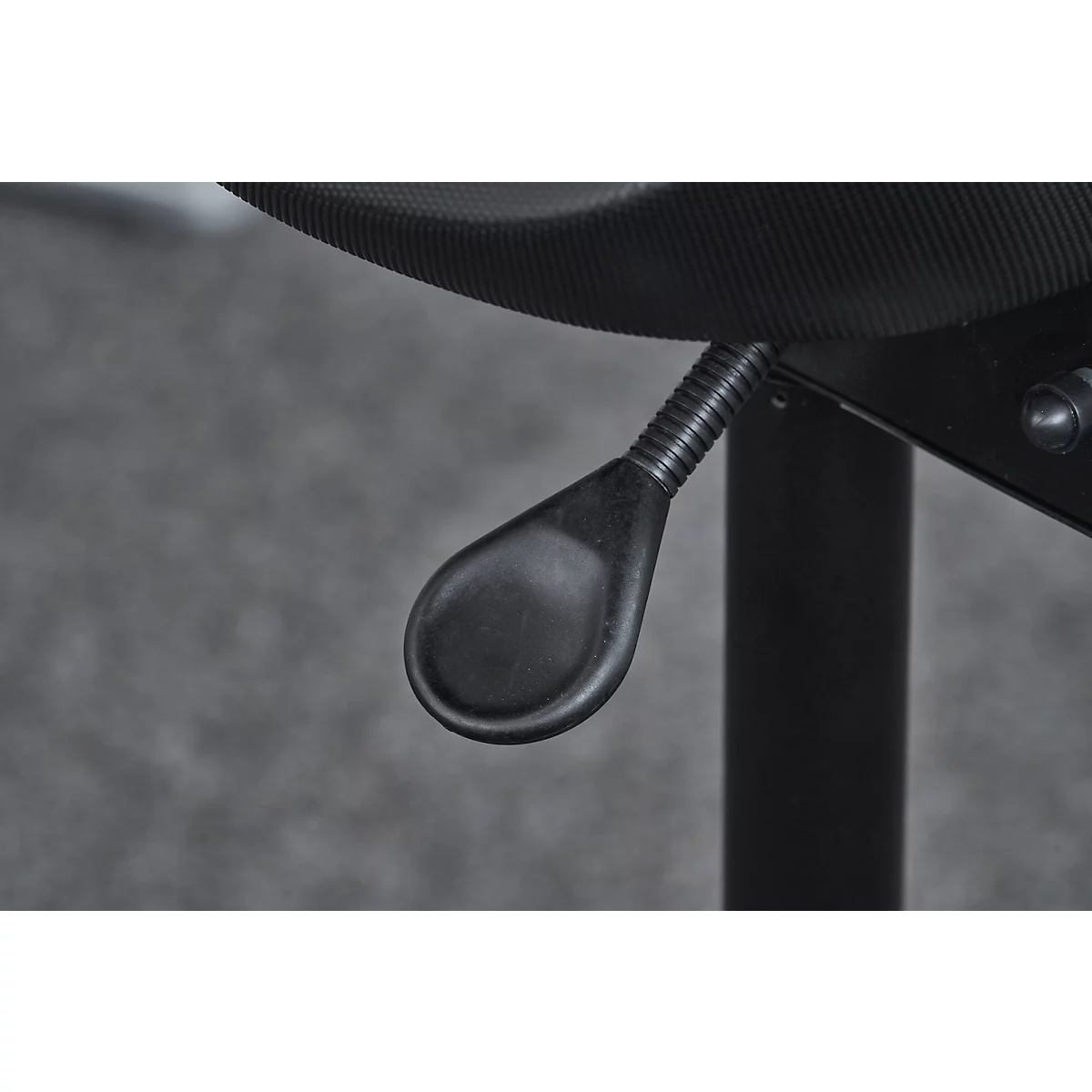 Close-up of the black, teardrop-shaped lever under a chair. Its position is attached to a corrugated metal spring.