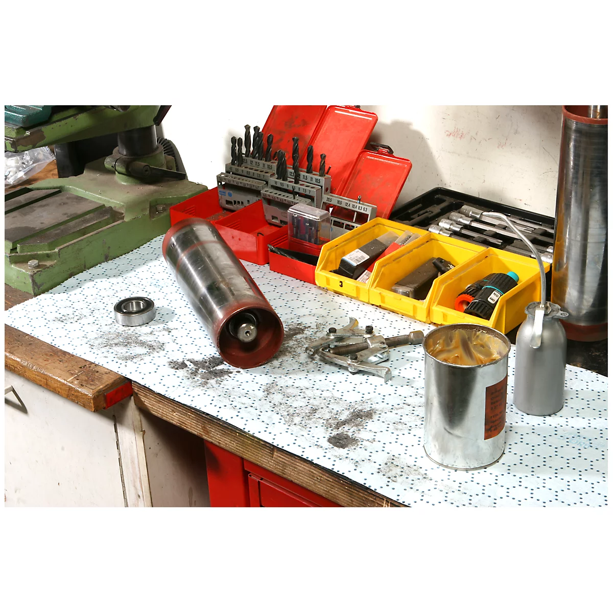 Zylinder und Werkzeug auf einer Werkbank. Ein Lager, eine Dose, Bohrer und eine Ölkännchen sind zu sehen.