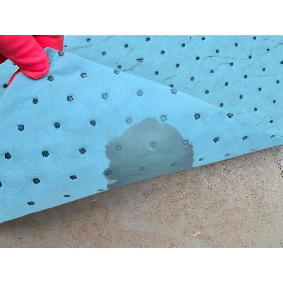 Light blue absorbent fleece with liquid stain and dotted pattern, held by a person with a red glove.