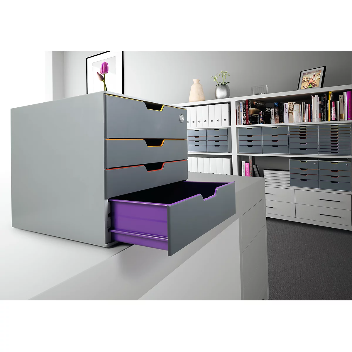 Meuble de bureau gris avec trois tiroirs. Le tiroir inférieur est partiellement sorti et de couleur violette.