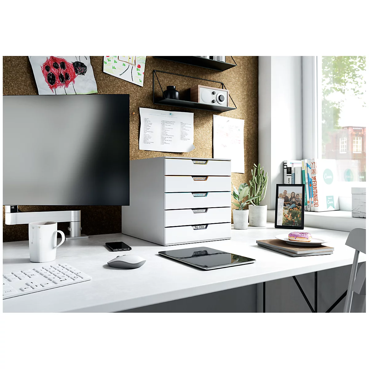 Bureau blanc avec caisson à tiroirs, moniteur, tablette et décor. Des notes sont accrochées au tableau d'affichage.