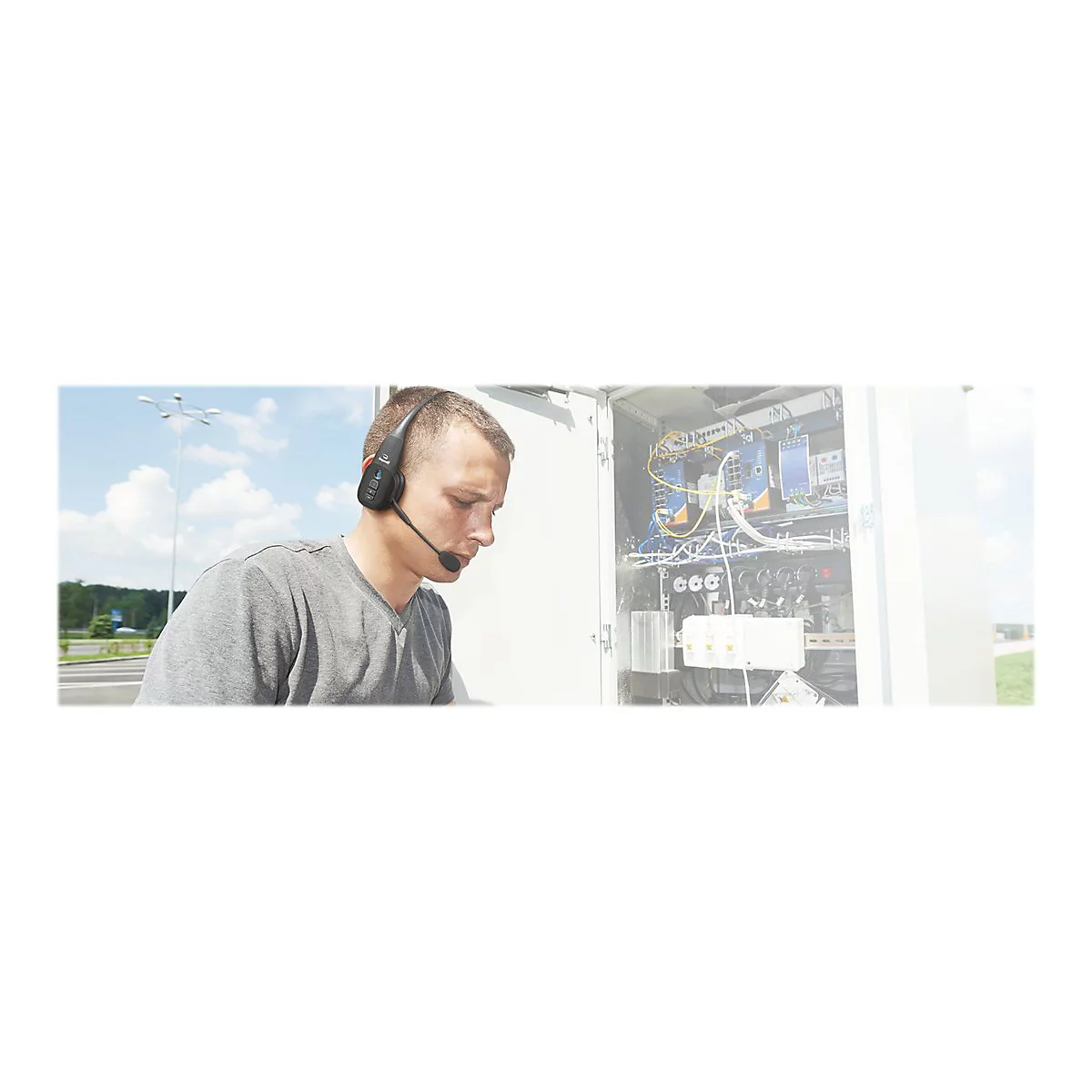 Ein Mann mit Headset, der an einem Schaltkasten arbeitet. Im Hintergrund sind Himmel und Straße zu sehen.