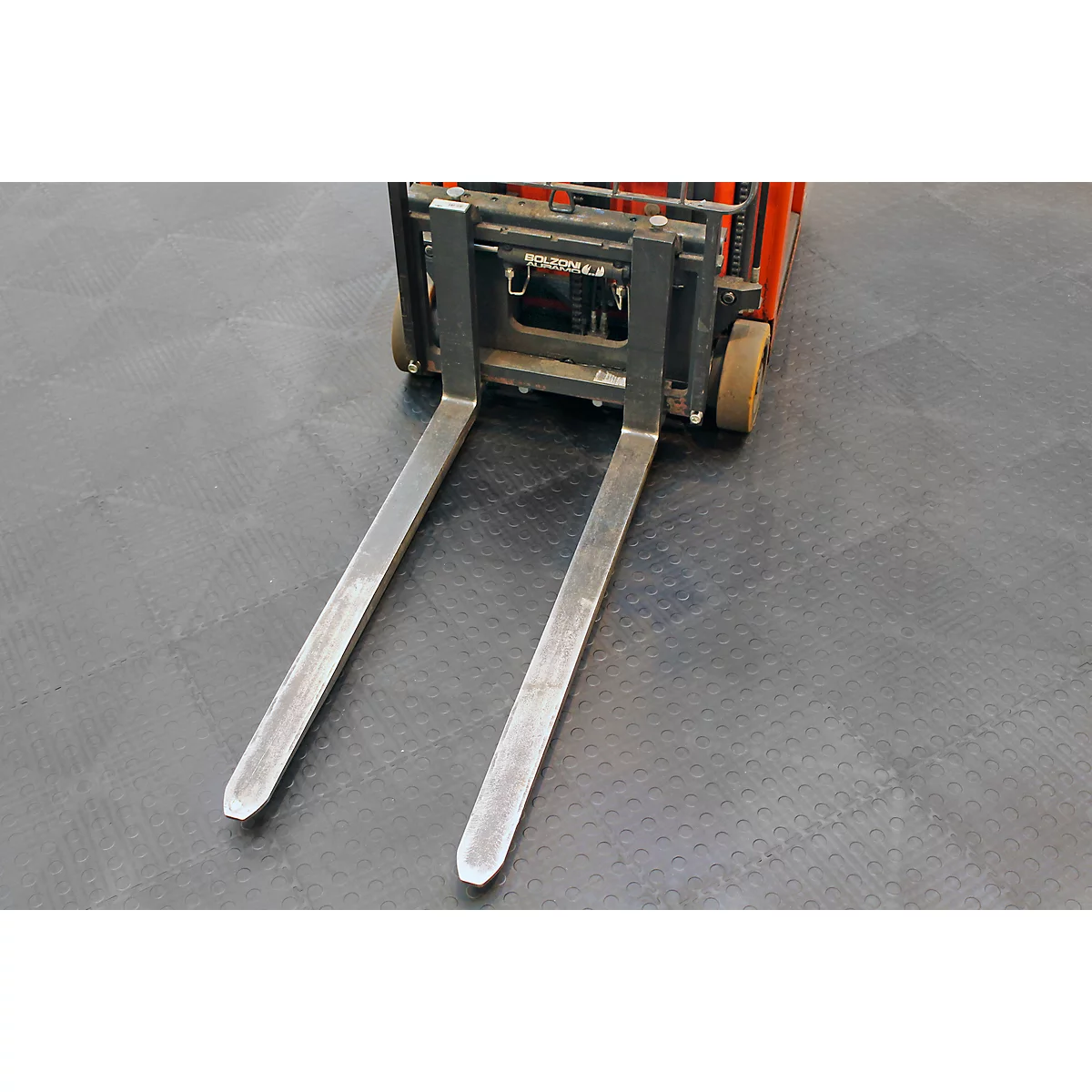 Nahaufnahme einer Gabelstaplergabel auf grauem Boden. Gabelzinken aus Metall, rot-schwarzer Stapler.