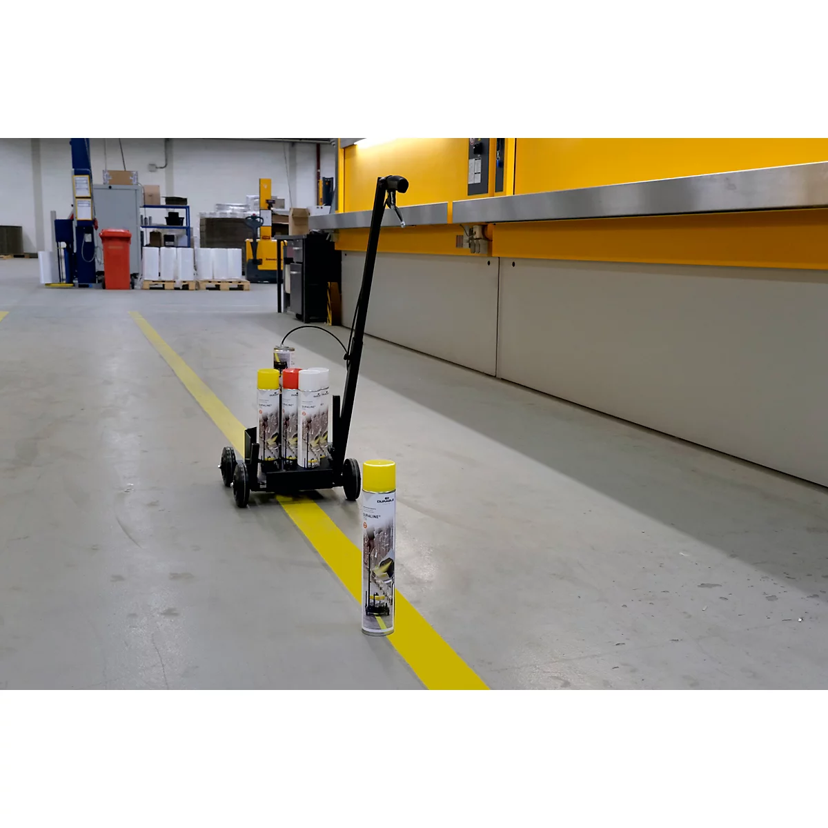 Gelbe Linie auf Betonboden mit Markierungswagen und Spraydose.