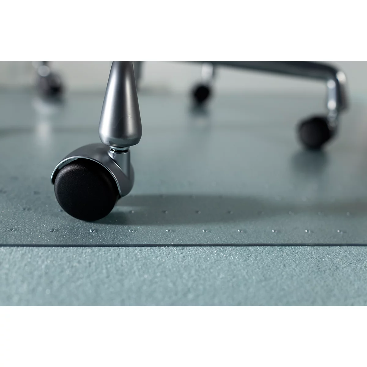 Nahaufnahme eines Stuhlrads mit schwarzem Rad auf einer blauen Bürostuhlmatte. Das Rad ist aus Metall gefertigt.