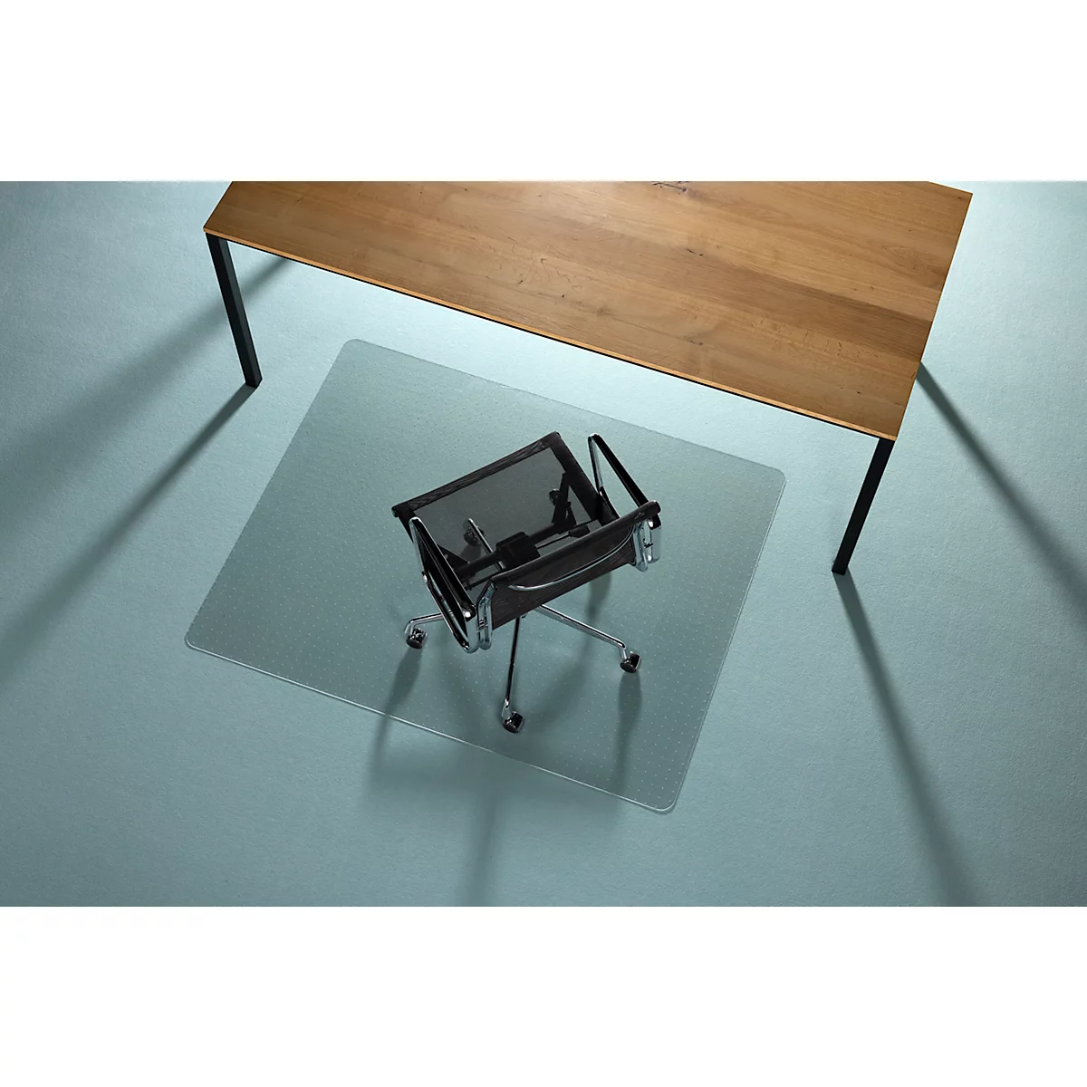 Bürostuhl mit transparente Bodenschutzmatte unter einem Holztisch.