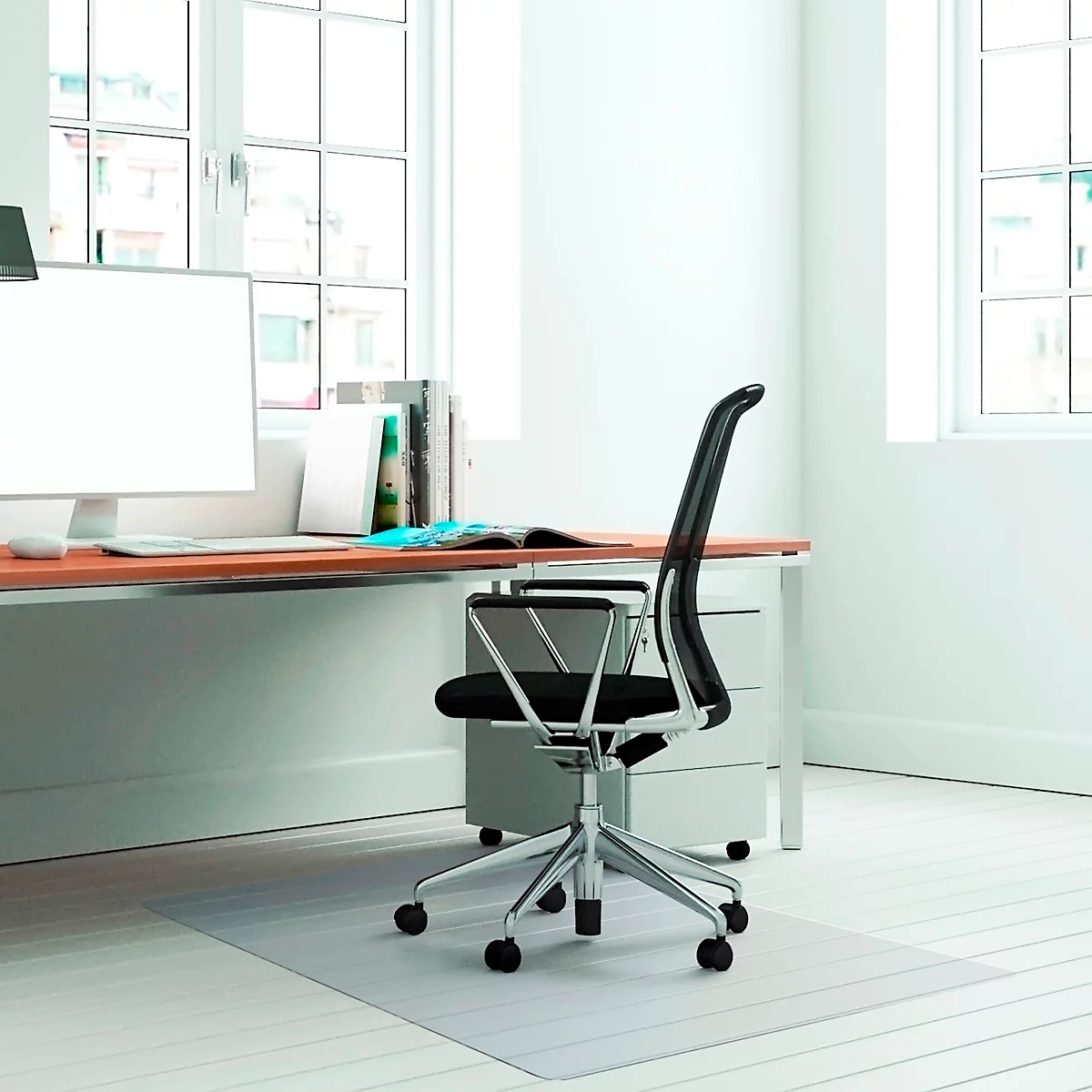 Büro mit Schreibtisch, Stuhl und Schreibtischunterlage. Fenster lassen Tageslicht herein. 