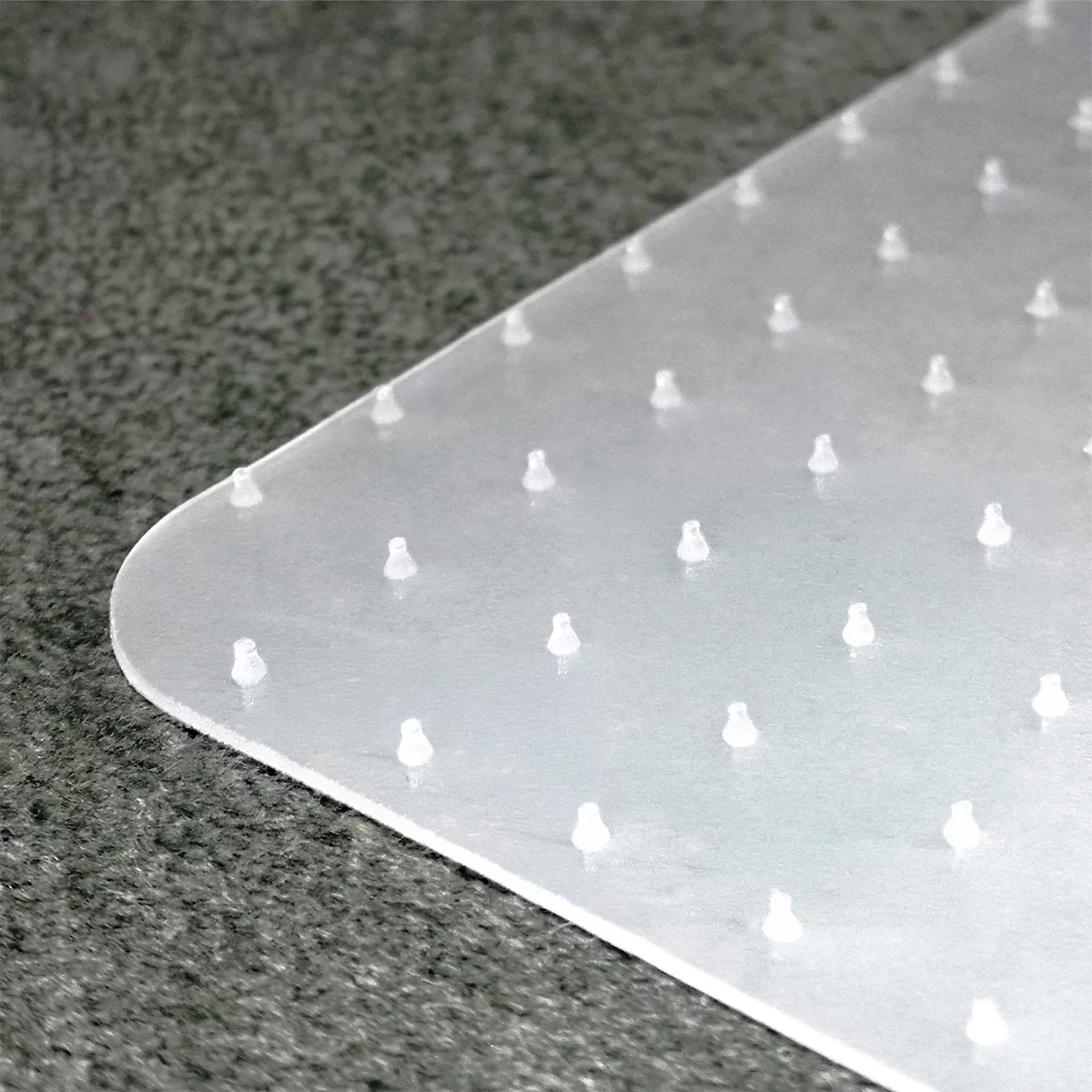 Nahaufnahme einer transparenten Bodenschutzmatte mit Noppen auf einem dunklen Teppichboden.