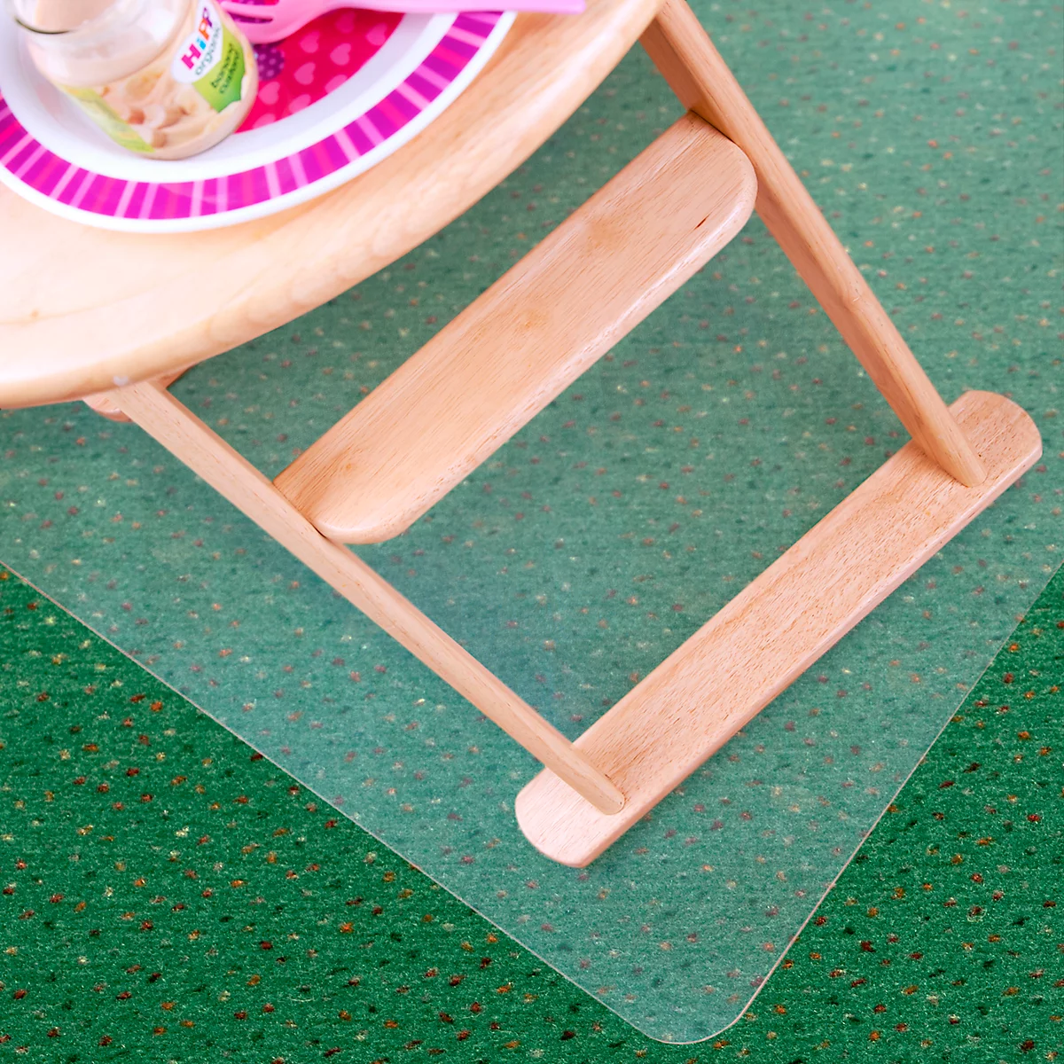 Detailaufnahme eines hölzernen Hochstuhls mit Essgeschirr auf grünem Teppich.