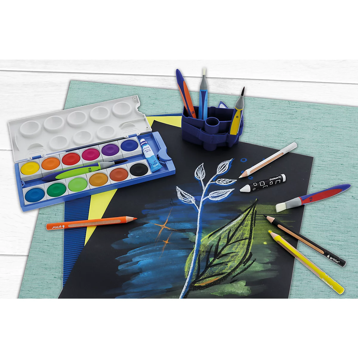 Une boîte de peinture, des crayons et un porte-crayons posés sur du papier coloré avec un dessin de feuille.