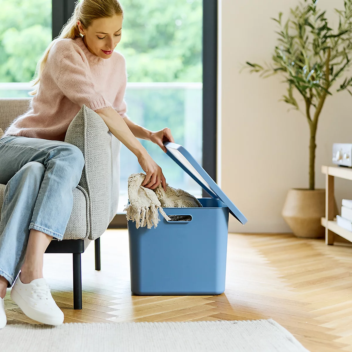 Boîte de rangement carrée bleue avec couvercle dans le salon. À côté d'un canapé, d'une fenêtre et d'une plante.