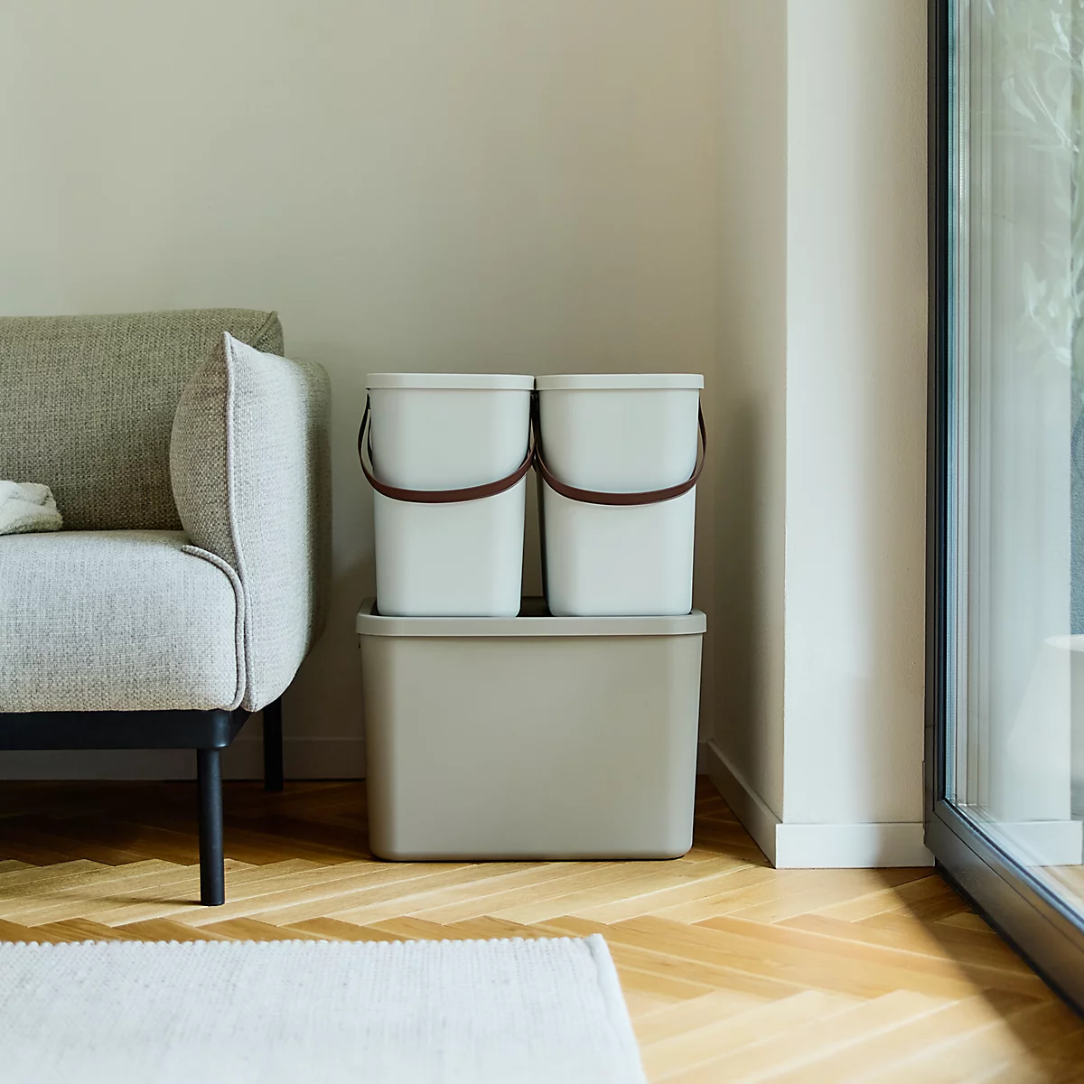 Boîte beige à côté d'un canapé. Parquet, tapis blanc et fenêtre en arrière-plan.