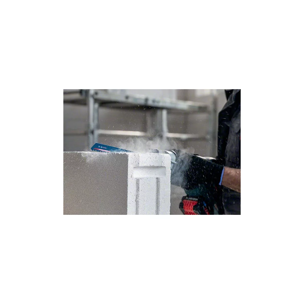 Eine Säge schneidet einen Gasbetonblock, Staubwolke entsteht.