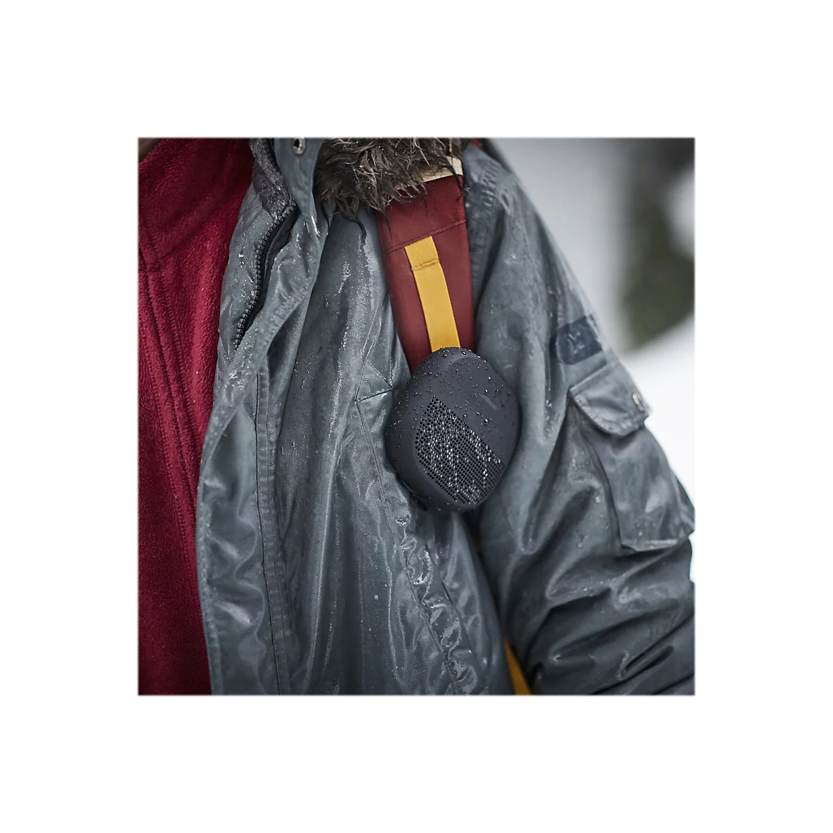 Ein Mann mit grauer Jacke und Kopfhörern im Regen. Auf der Schulter ein Kopfhörer.