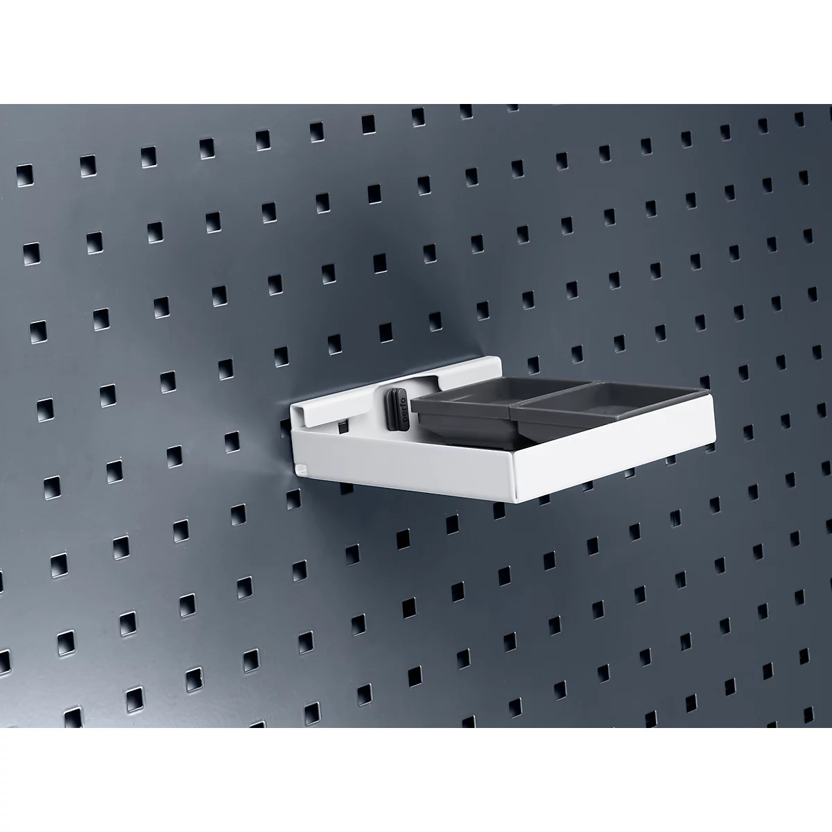 Eine weiße Ablage mit schwarzer Unterteilung an einer Lochwand. Sie ist mit schwarzen Fächern bestückt.