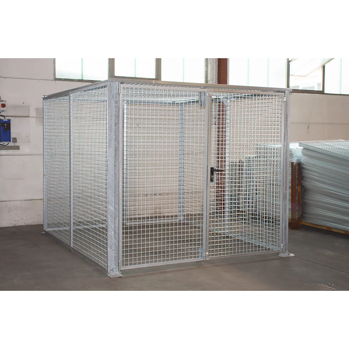 Une cage métallique carrée avec une porte et une serrure. Elle se trouve dans un hall.