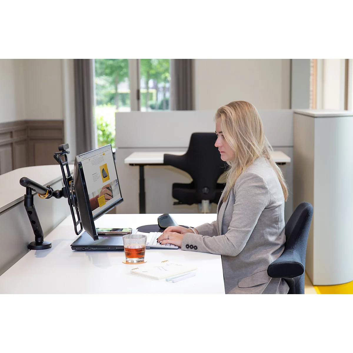 Une femme dans un bureau travaille sur un ordinateur. Elle tape sur un clavier, un verre de liquide est sur la table.