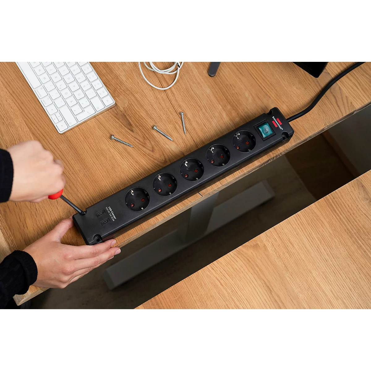 Dunkle Steckerleiste mit Netzkabel; vier Steckdosen, Befestigungslöcher.