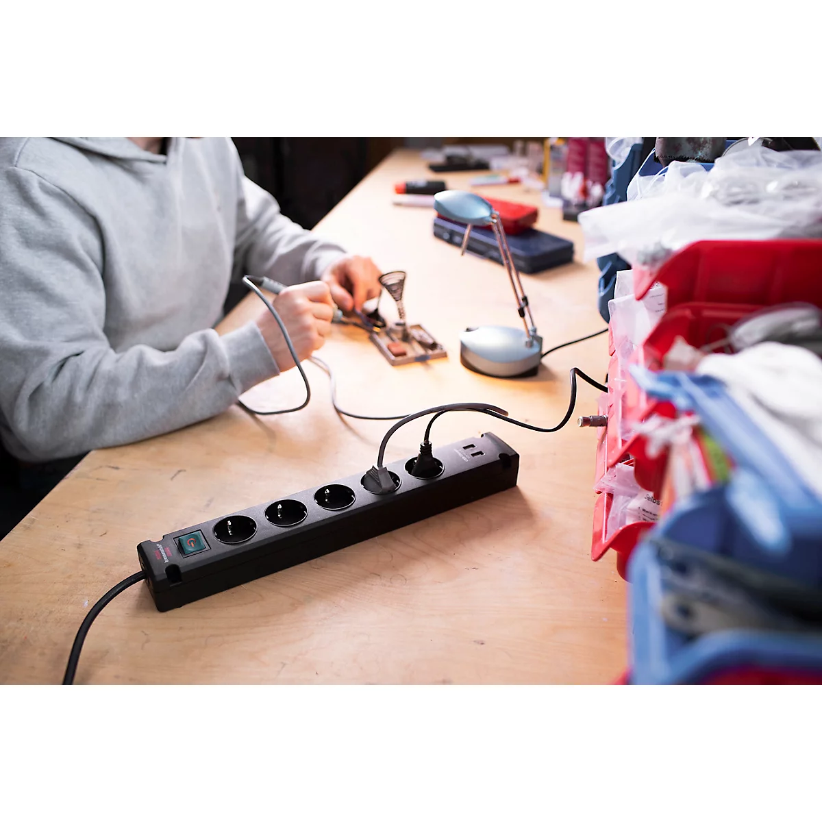 Personne soudant de l'électronique, multiprise avec câbles sur une table en bois, boîte à outils.