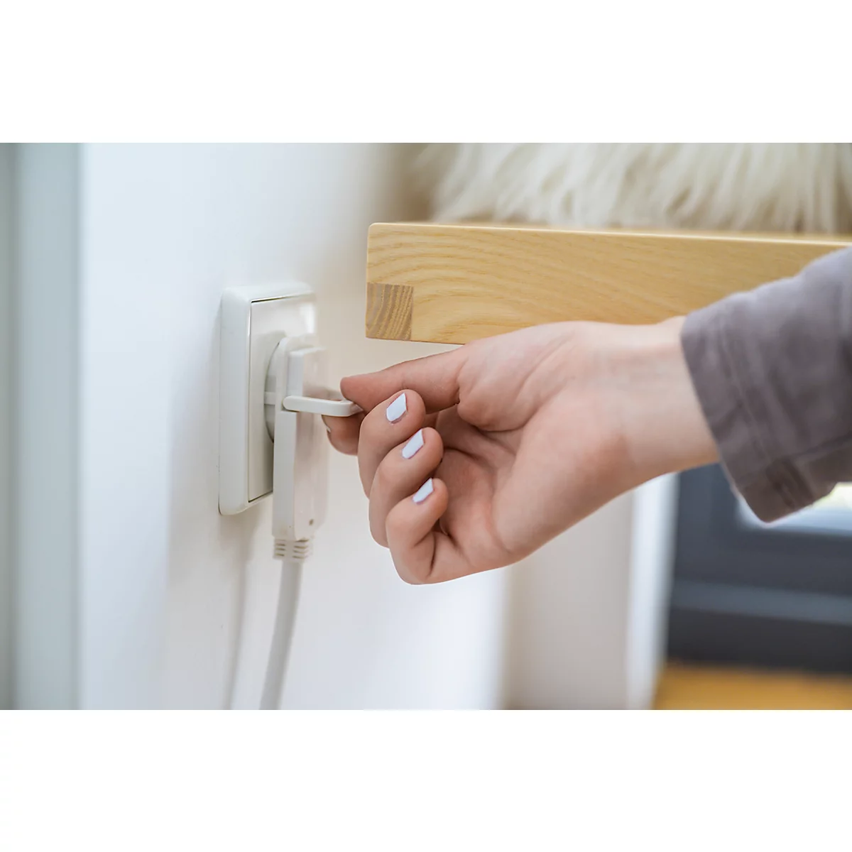 Une main retire une prise de la prise de courant. La main a les ongles vernis. La prise est sur un mur blanc.