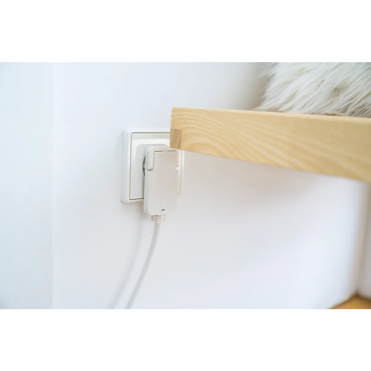 Prise murale blanche avec un adaptateur branché et un câble. Une étagère en bois est partiellement visible en arrière-plan.