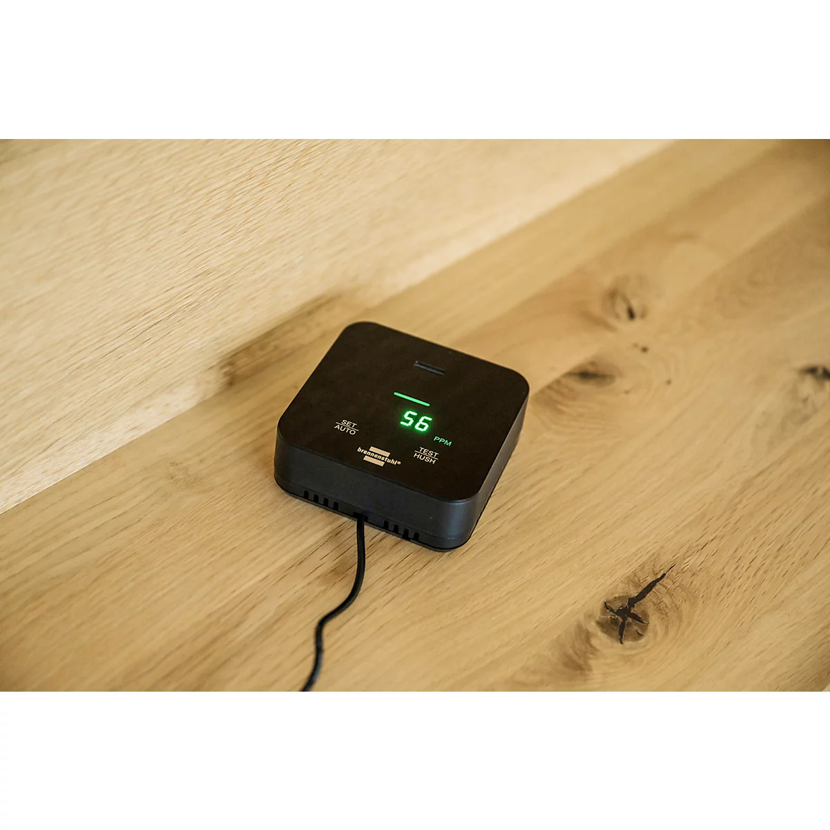 Zwart vierkant apparaat met groene display: 56. Op houten oppervlak met kabel.