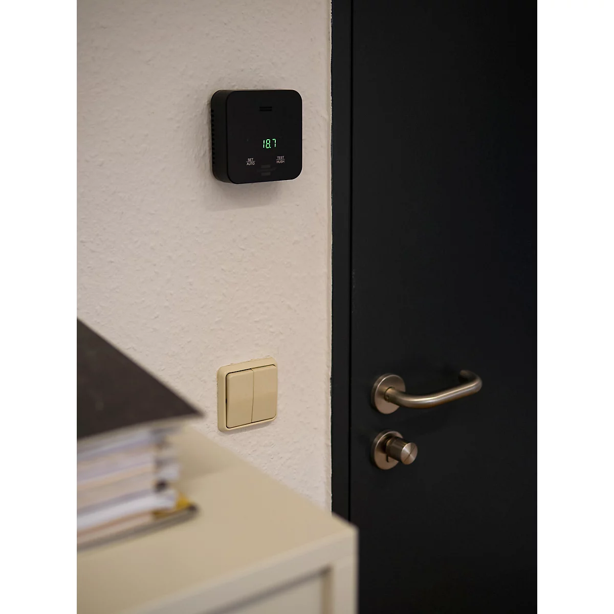 Achterkant van een zwart, vierkant apparaat met een cirkelvormige uitsparing en een haak om op te hangen.