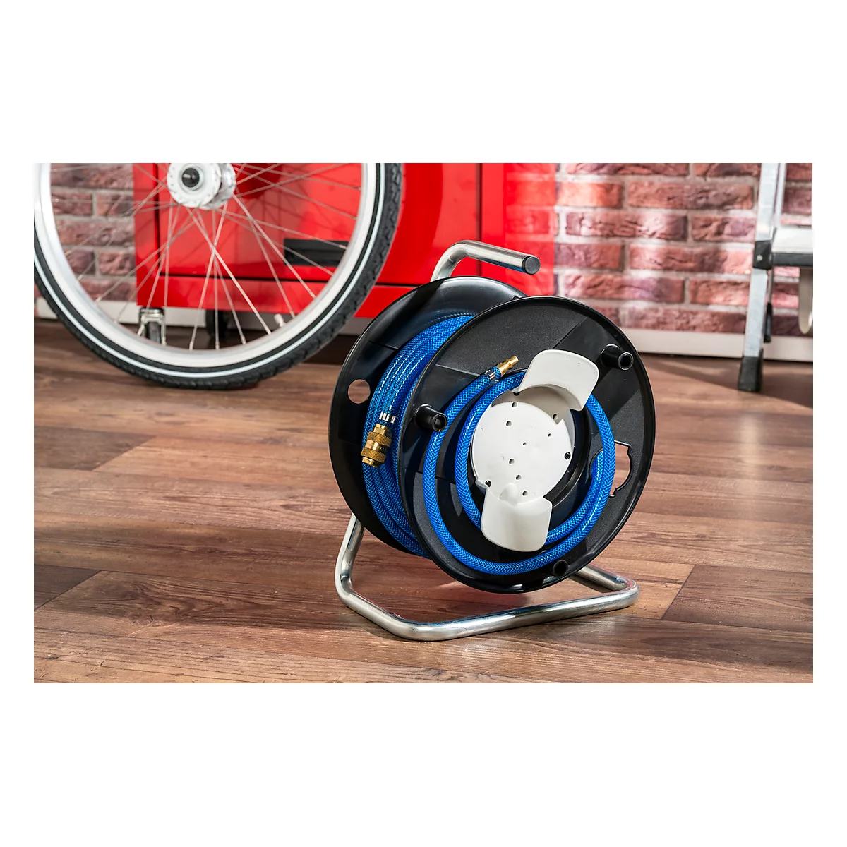 A blue garden hose reel with a metallic frame. In the background, a bicycle and a brick wall are visible.