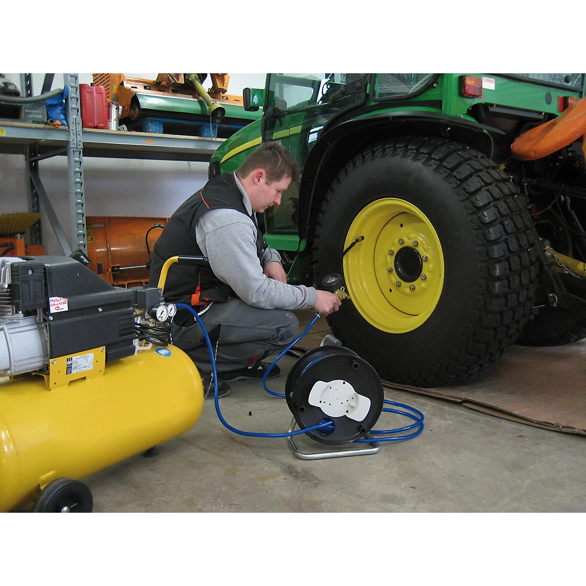 Man inflating tractor tire with compressed air. Yellow compressor and green tractor in the background.