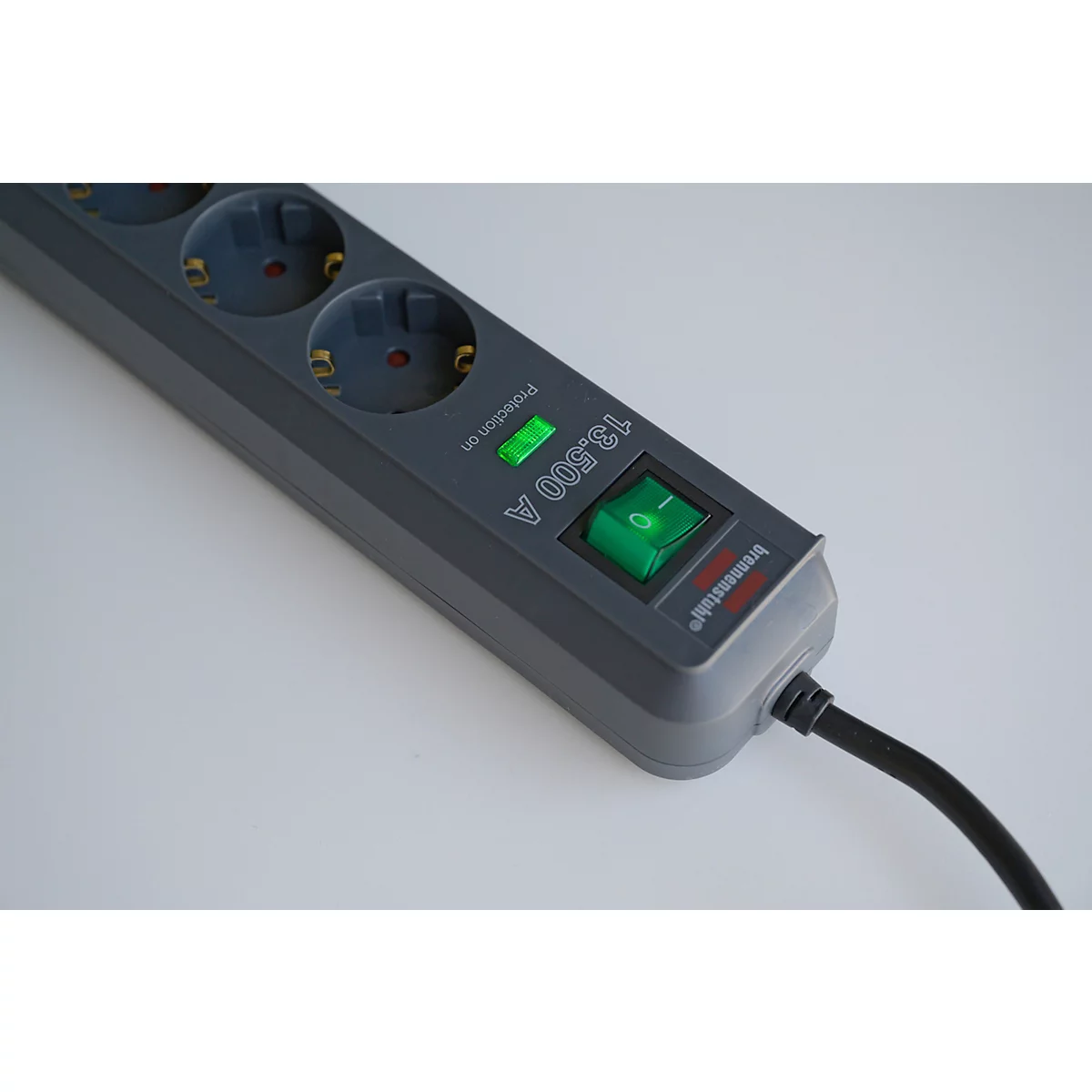 Graue Mehrfachsteckdose mit grünem Schalter und Kontrollleuchte. Schwarzes Kabel ist angeschlossen.