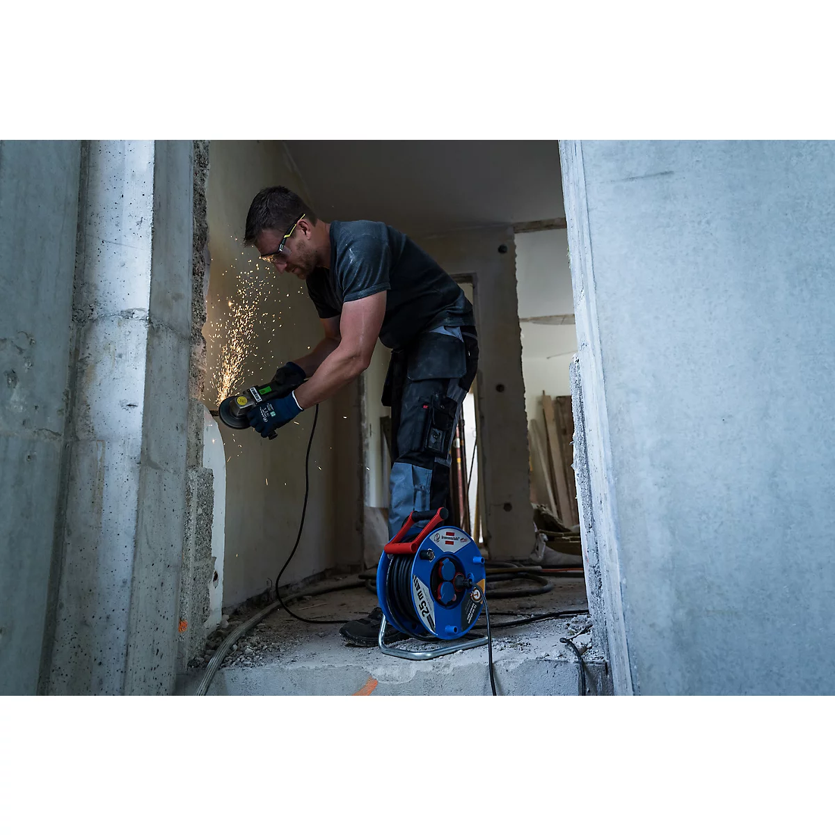 Un homme coupe un mur en béton avec une meuleuse d'angle, des étincelles volent. Une pièce en arrière-plan. Travaux de construction.