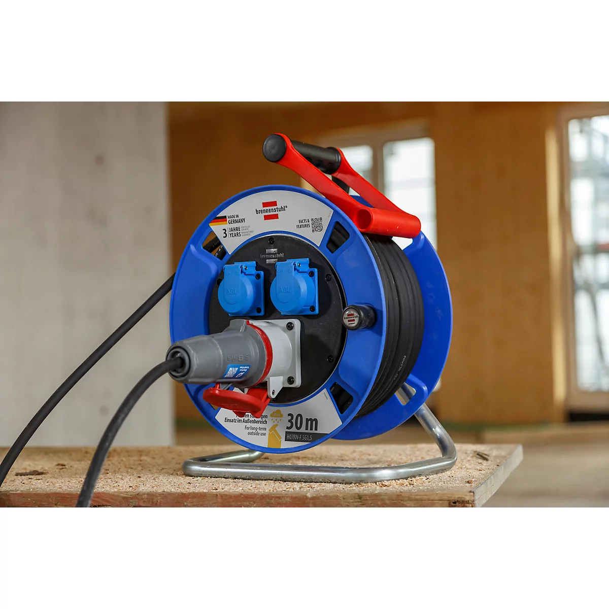 Kabeltrommel mit rotem Griff, blauen Seiten und schwarzem Kabel. Grau-roter Stecker.