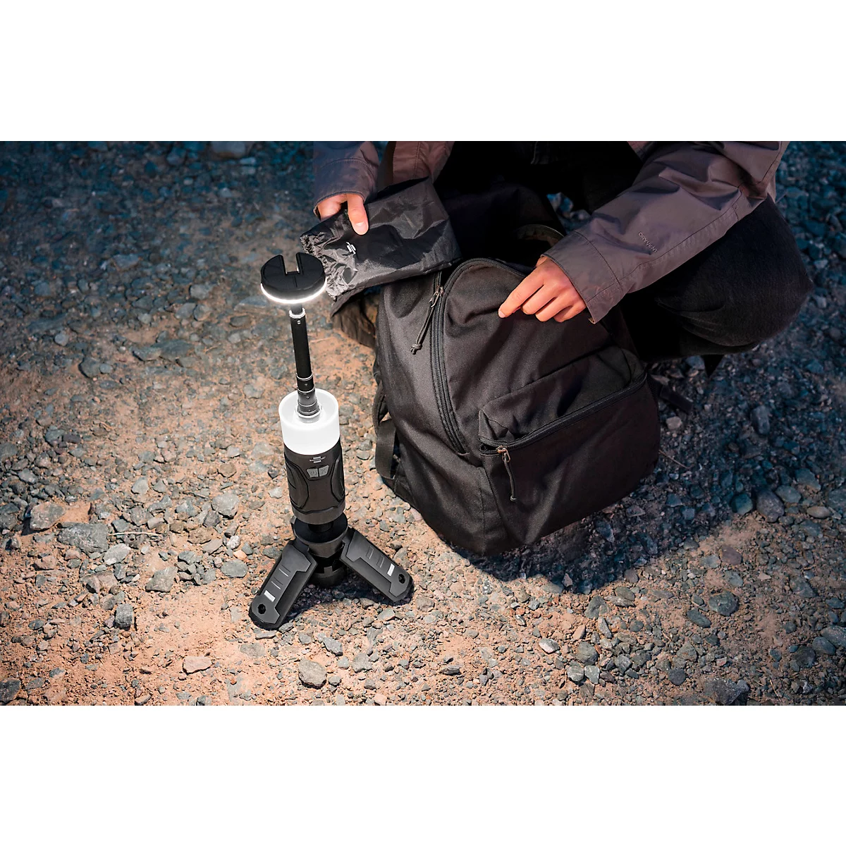 Une lanterne LED noire et cylindrique avec un élément lumineux blanc. Il y a des boutons et une bande grise sur le côté.