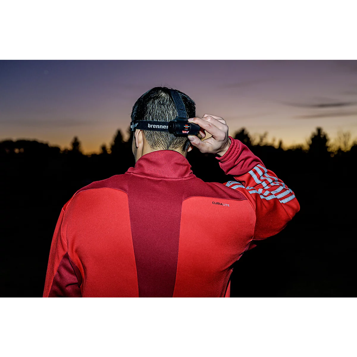 Un homme souriant avec une barbe et un casque de chantier, lampe frontale éclairée.
