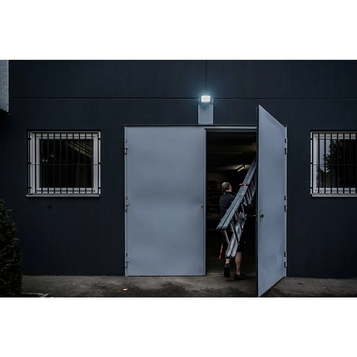 Une personne installe un projecteur LED noir sur un mur.