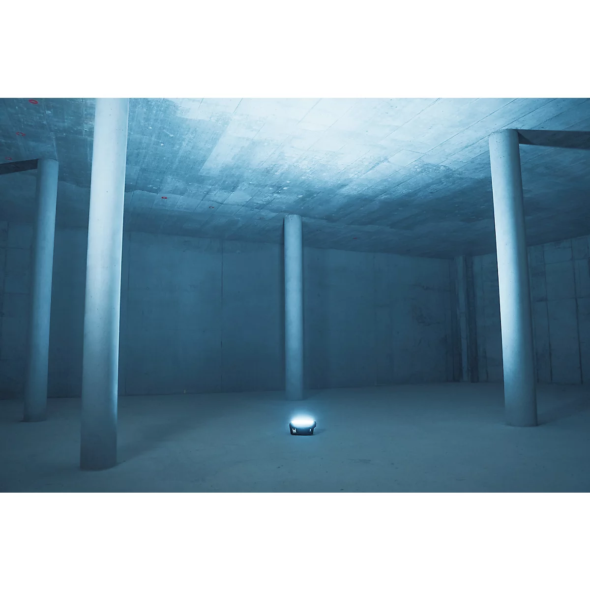 Pièce grise et vide avec des piliers en béton, une source de lumière au sol.