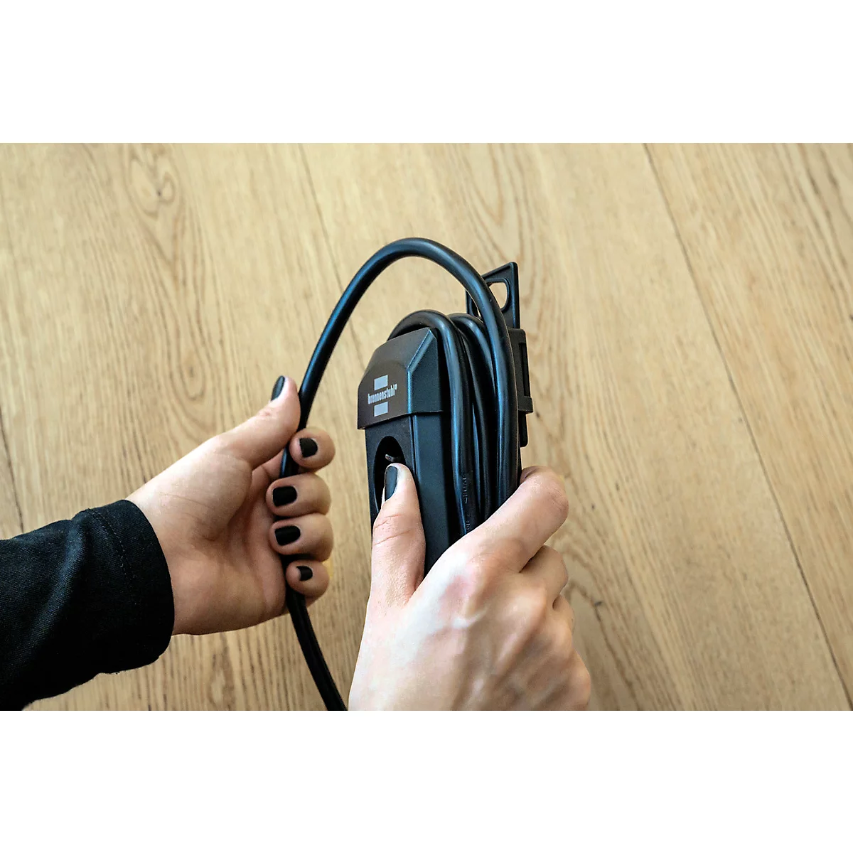 Mains tenant un câble de chargement noir pour une voiture électrique. Le fond est un plancher en bois.