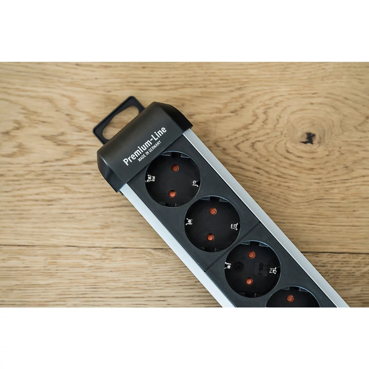 Een zwarte Premium-Line stekkerdoos met vier stopcontacten, ligt diagonaal op hout. Opschrift: Premium-Line, Made in Germany.