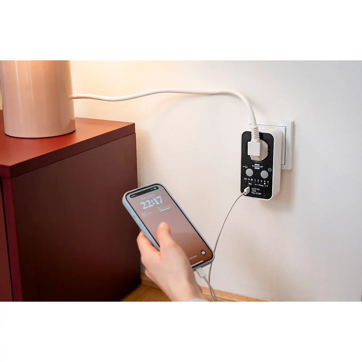 Un smartphone se charge à partir d'une prise murale. L'heure 22:17 est visible sur l'écran.