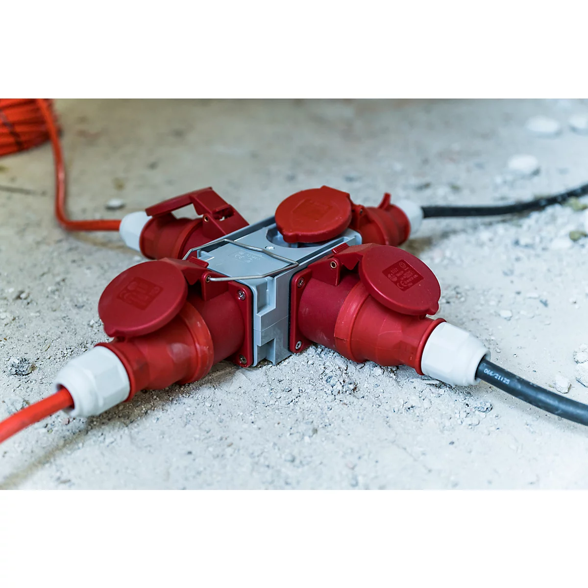 Un connecteur industriel rouge et gris sur fond noir. Il comporte des couvercles à charnières, une poignée et des ouvertures rondes.