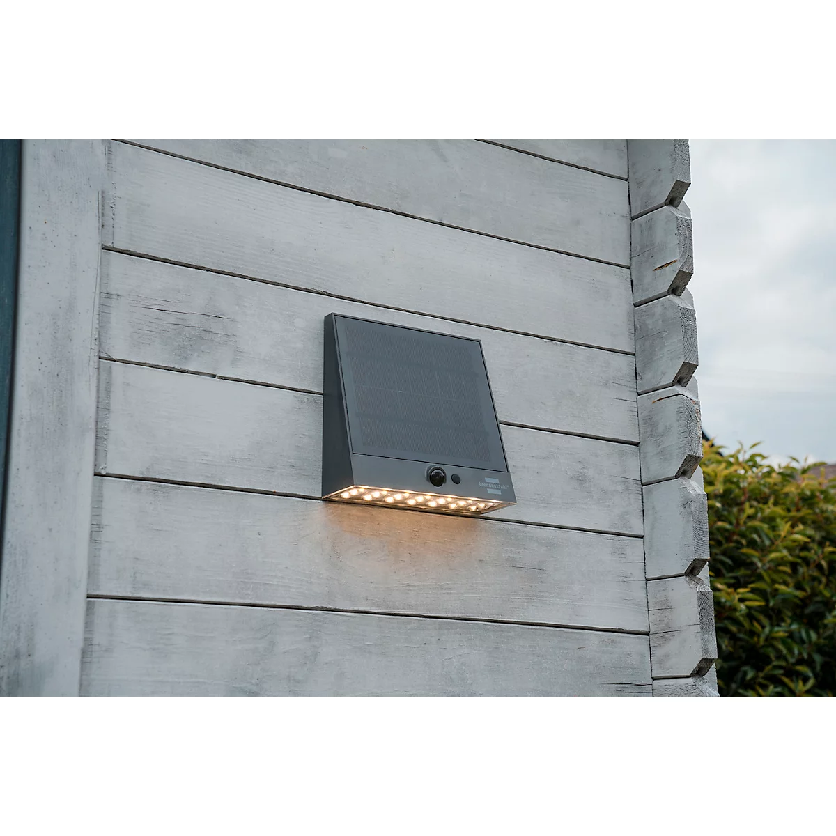 Applique murale sombre avec panneau solaire montée sur façade en bois, émettant de la lumière. 